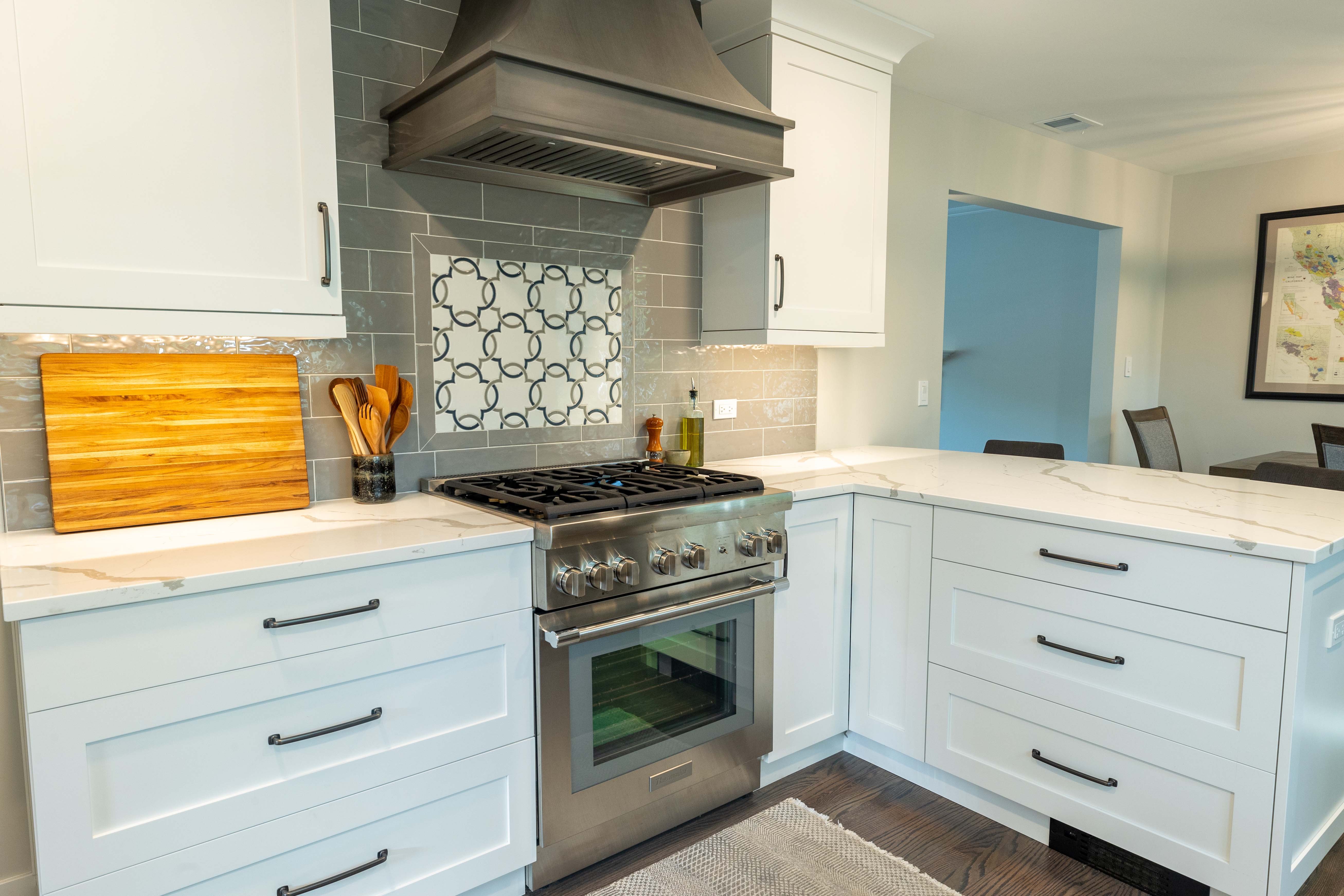 Kitchen with white cabinets and peninsula with quartz countertop and feature backsplash under the range 