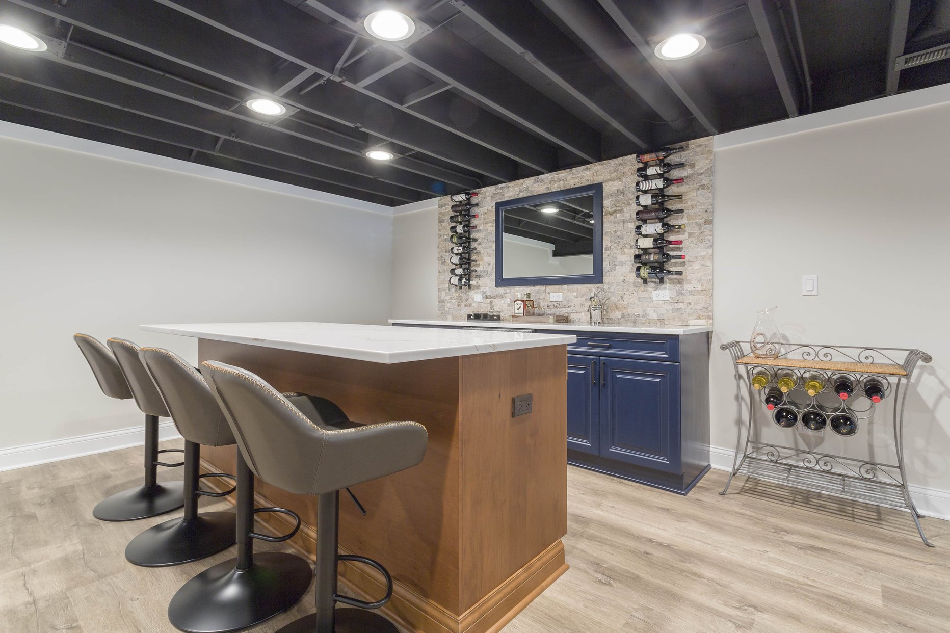 Blue full stocked bar with brown island and leather bar stools in a finished basement with wood floors. 