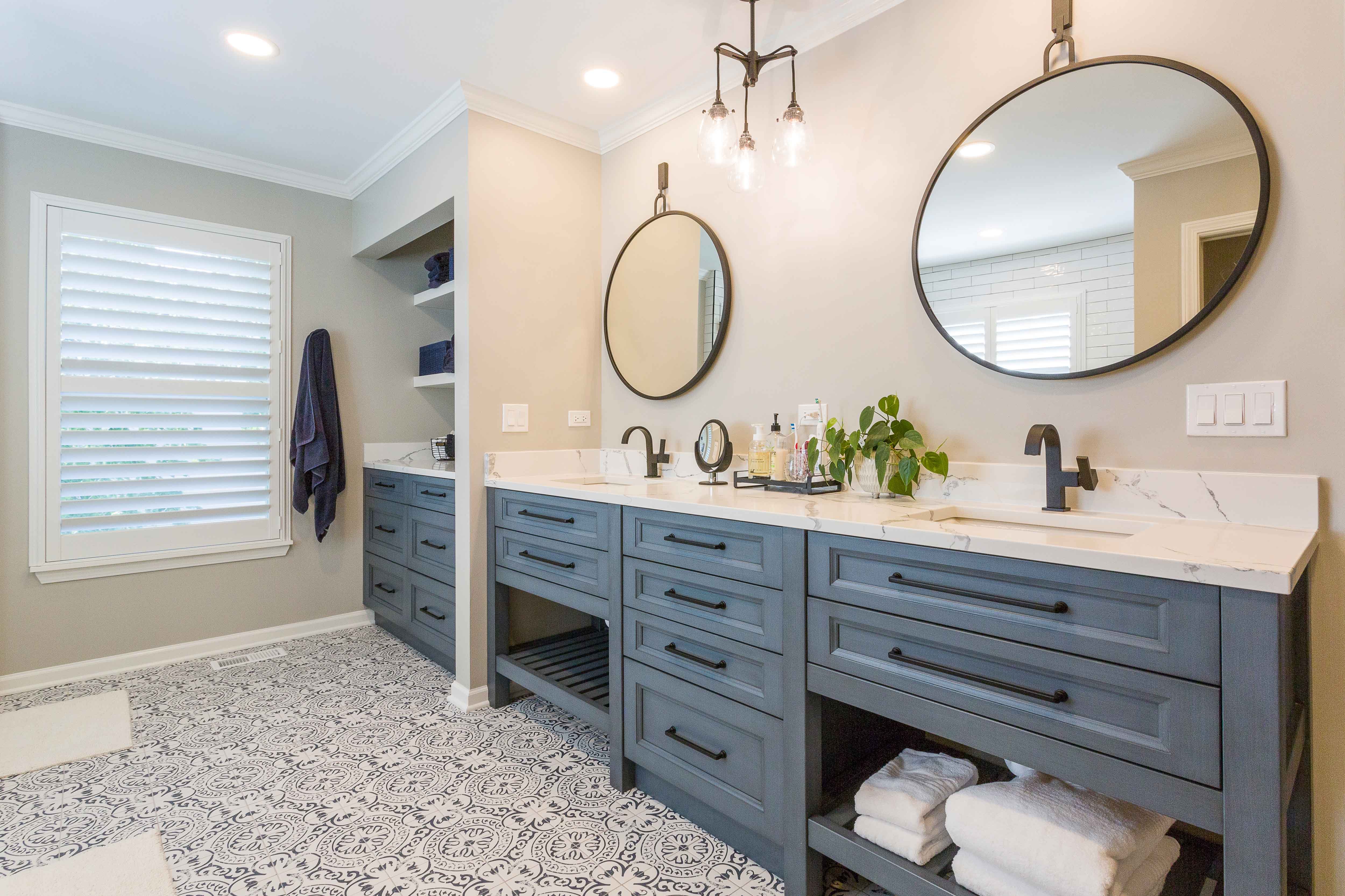 Blue Console vanity with a painted tile on  the floor. Built-in storage for towels, two round mirrors, and two rounded short, single handles faucets complete the double vanity. 