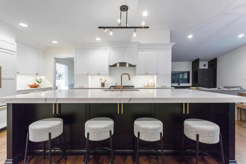 large kitchen island with white marble countertops, four stools, and gold hardware