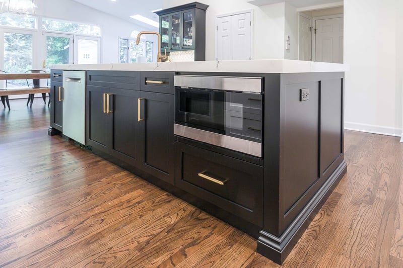 Large black kitchen island with gold hardware, marble countertop, and built in microwave
