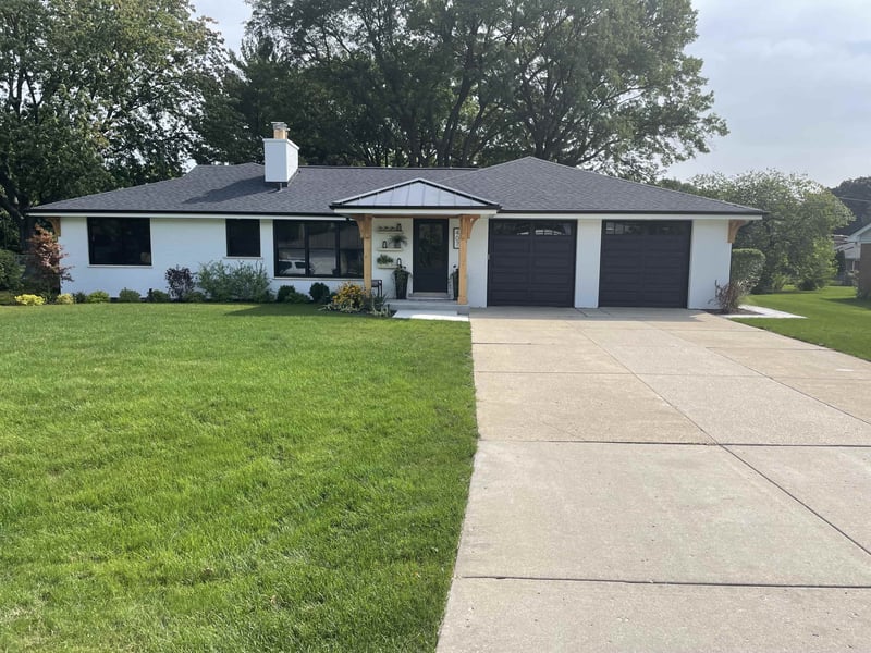 the front of a farmhouse style home with white wash brick, wood pillars and black garage doors 