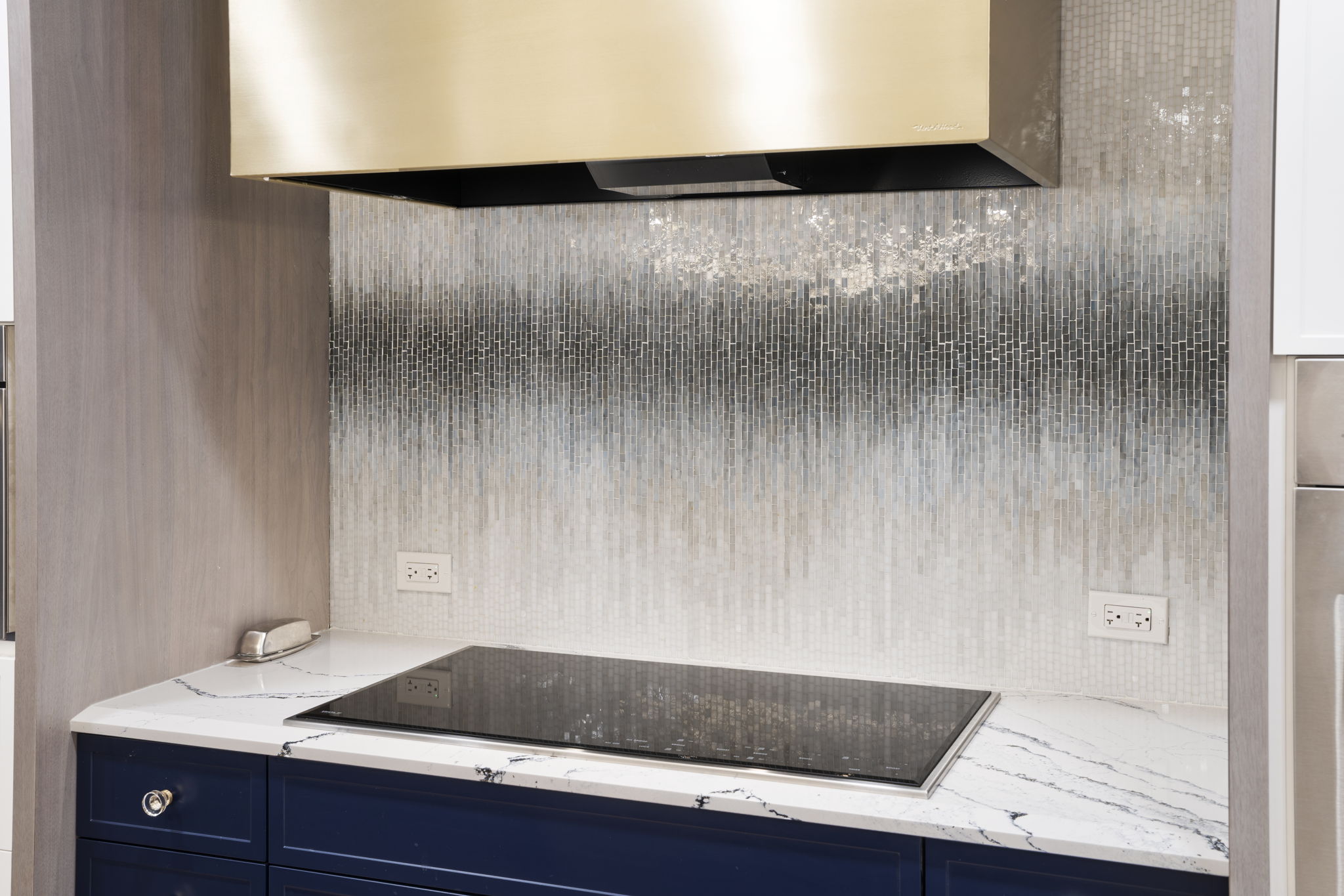 Range wall with billie mosaic glass tiles in grey and a gold hood 
