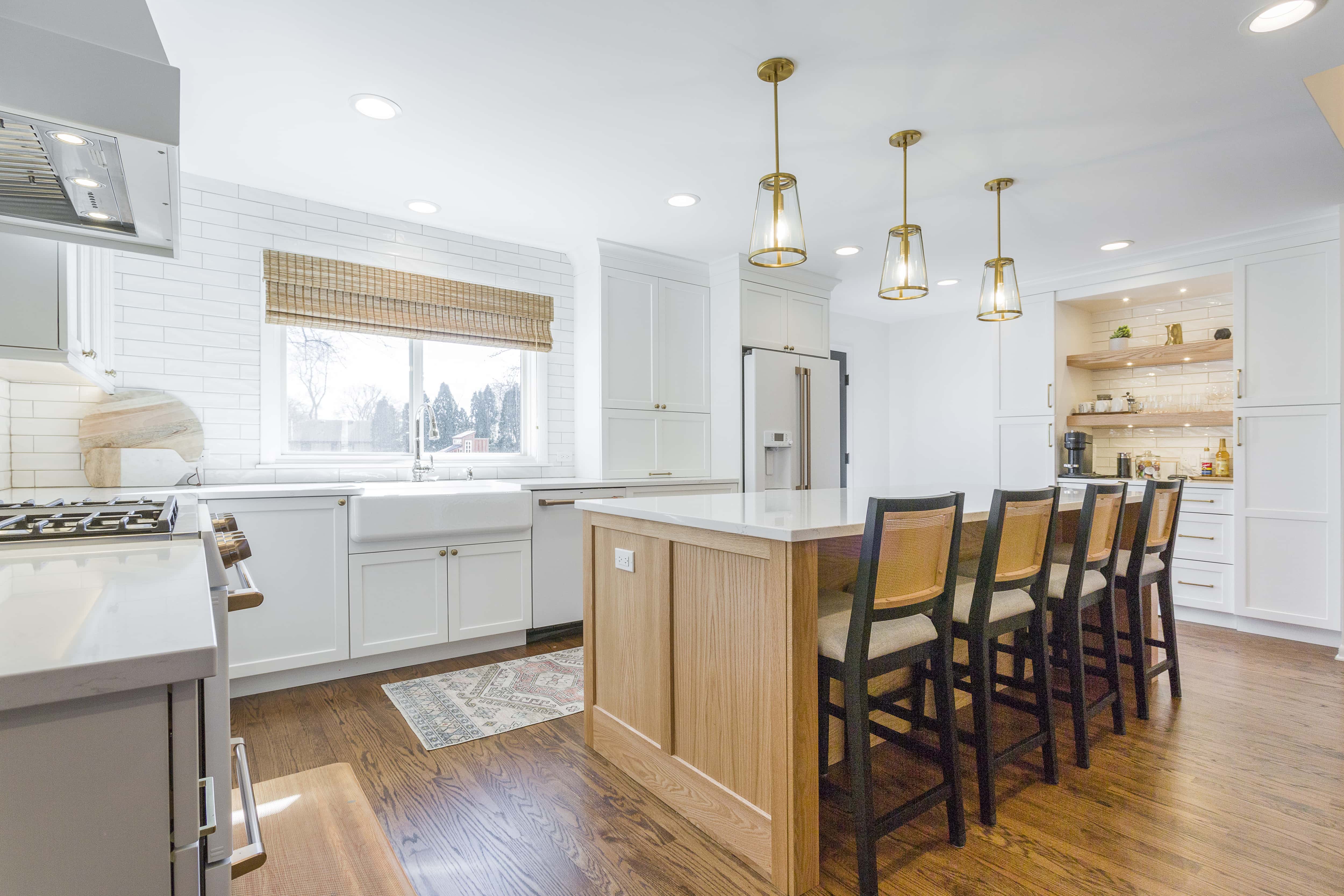 Large open kitchen with white cabinets, gold hardware, natural wood accents, and copious natural light from the window above the sink. 