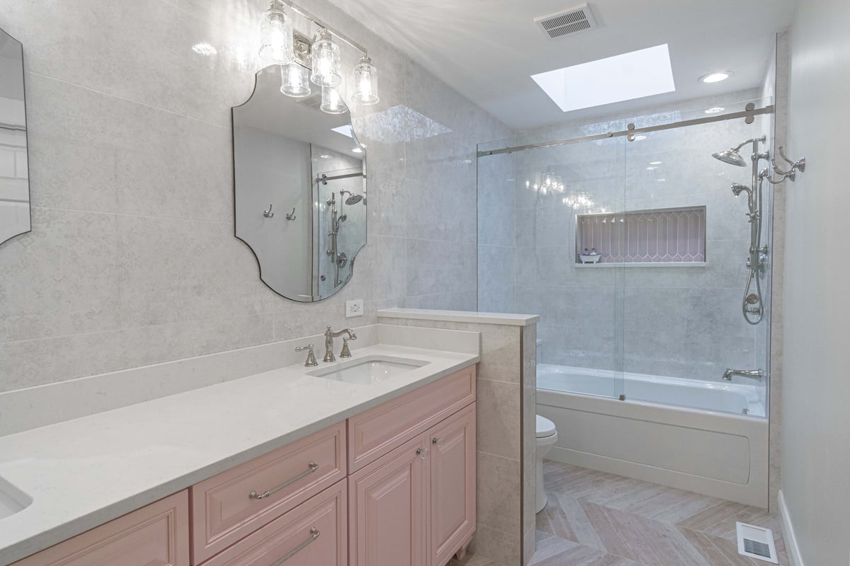 Bathroom with beige walls pink cabinets and elegant vanity mirror bathtube with glass lsiding door 