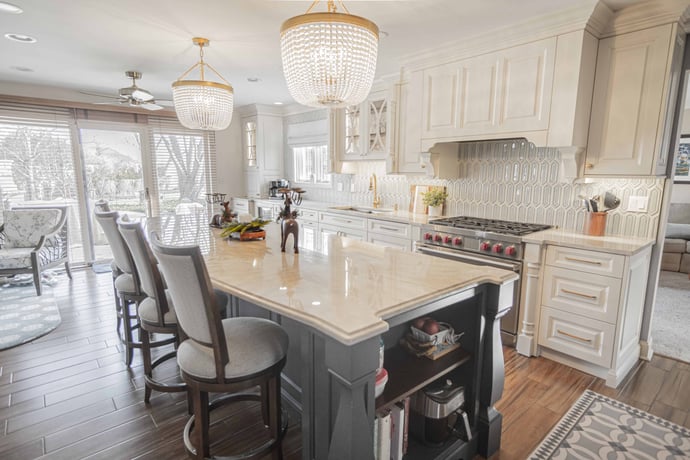 Elegant kitchen with gold and clear chandeliers white cabinets and light blue island. 