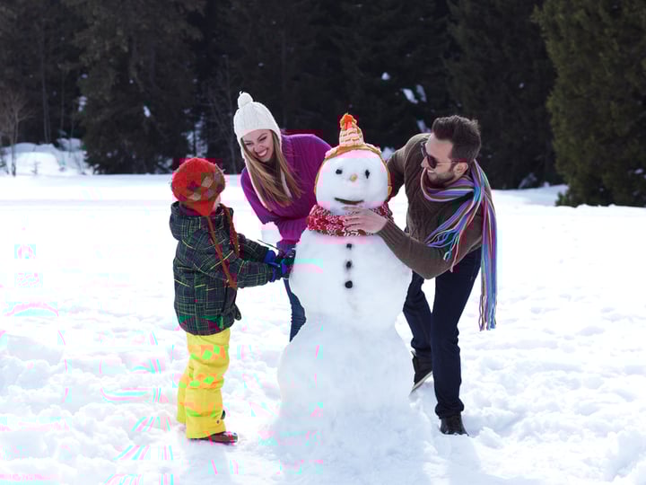 happy young family playing in fresh snow and making snowman at beautiful sunny winter day outdoor in nature with forest in background